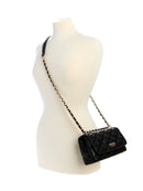 A black quilted leather shoulder bag with a gold-tone chain strap, displayed on a cream-colored mannequin torso against a white background.