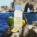 Dolce & Gabbana perfume bottle with an apple and lemon on rocks by the sea